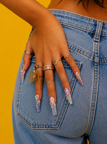 Hand with colorful nail art and multiple rings on a yellow background