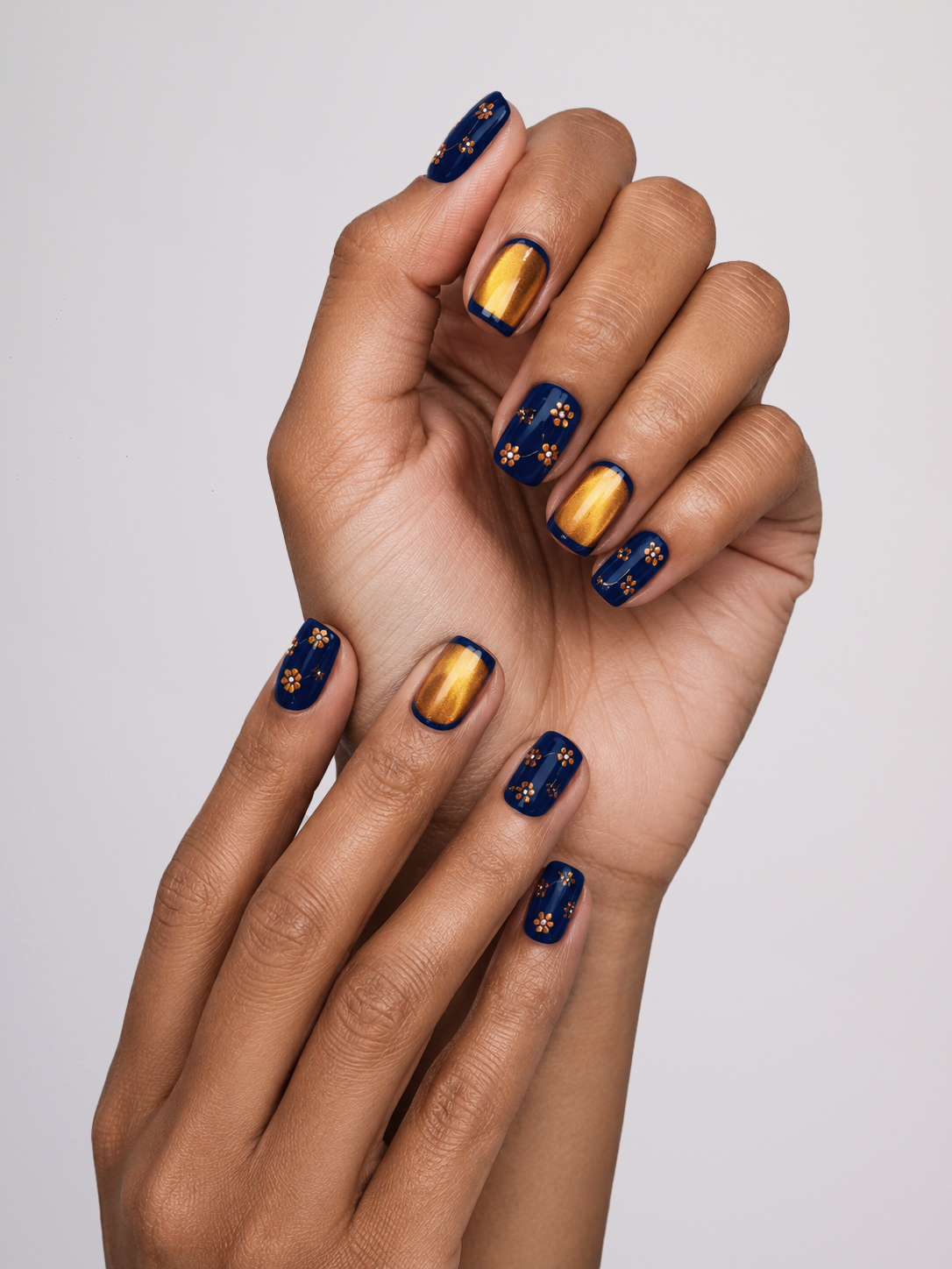 A close-up of a person's hands showcasing a manicure with navy blue and metallic gold nail art.