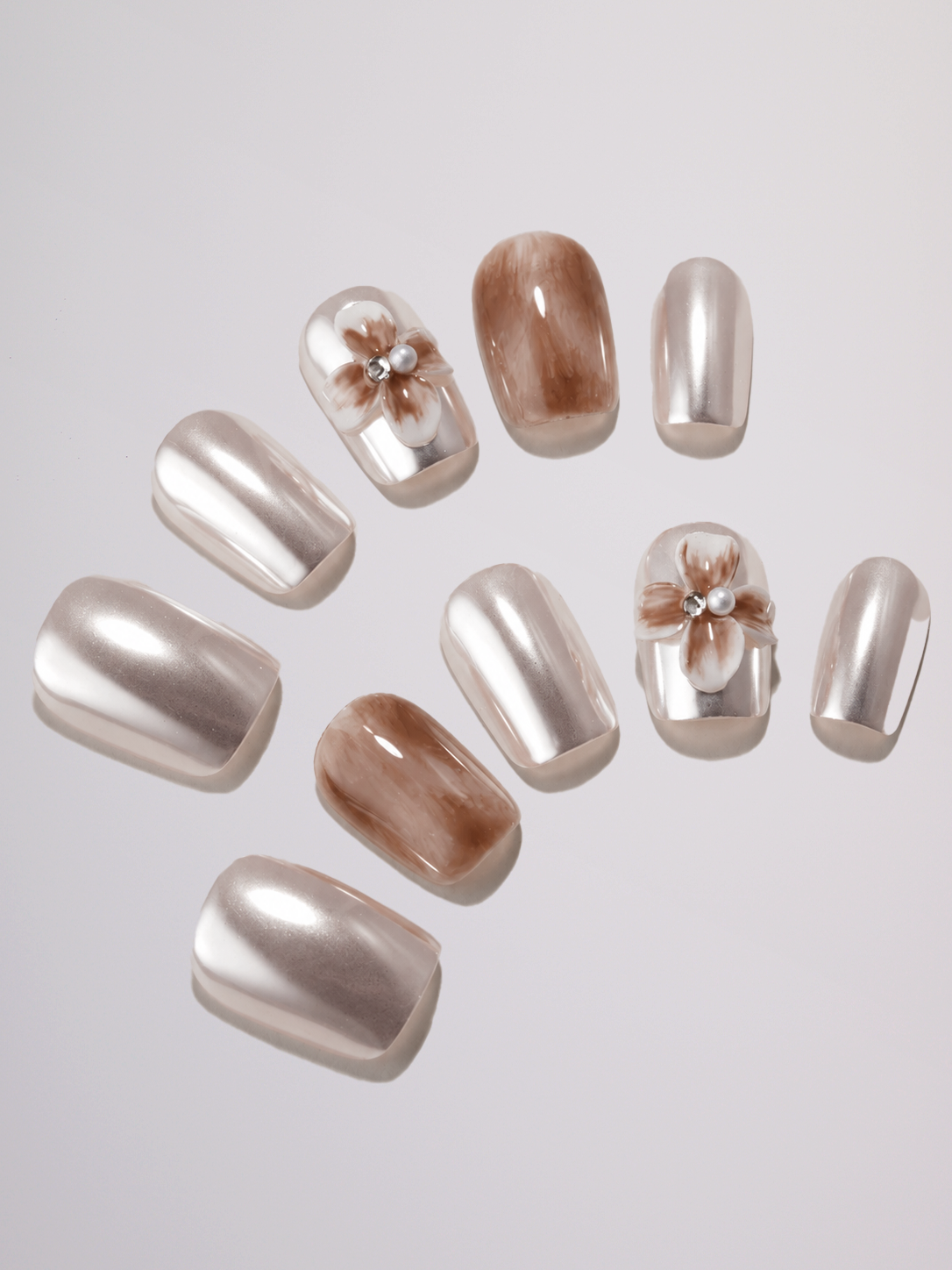 A close-up of a person's hands wearing a white long-sleeve blouse, silver metallic nail polish, and a large gold ring, set against a plain light gray background.