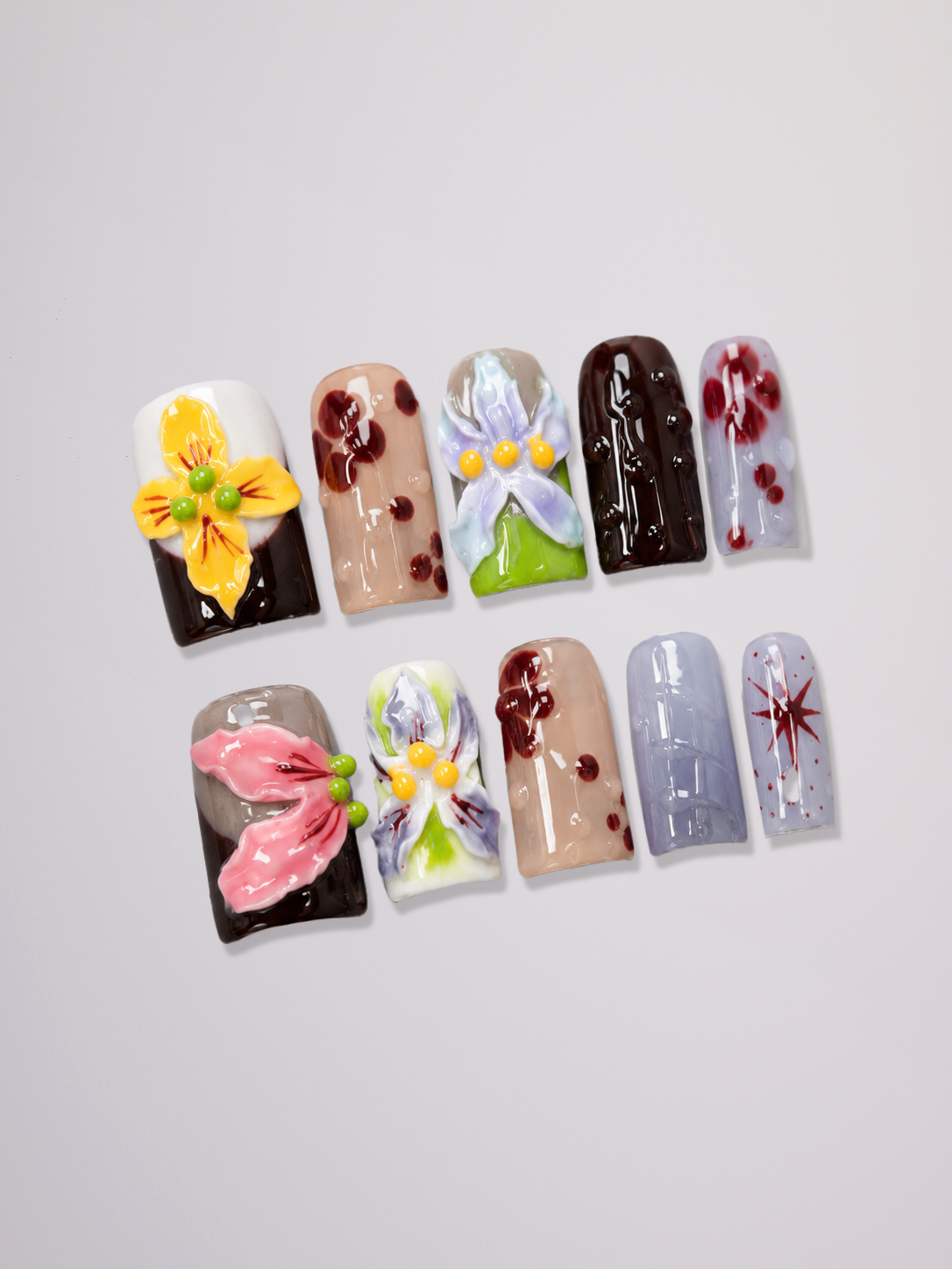 A close-up of a hand displaying a variety of colorful nail art designs, including glitter, floral patterns, and abstract gradients, set against a plain light gray background.