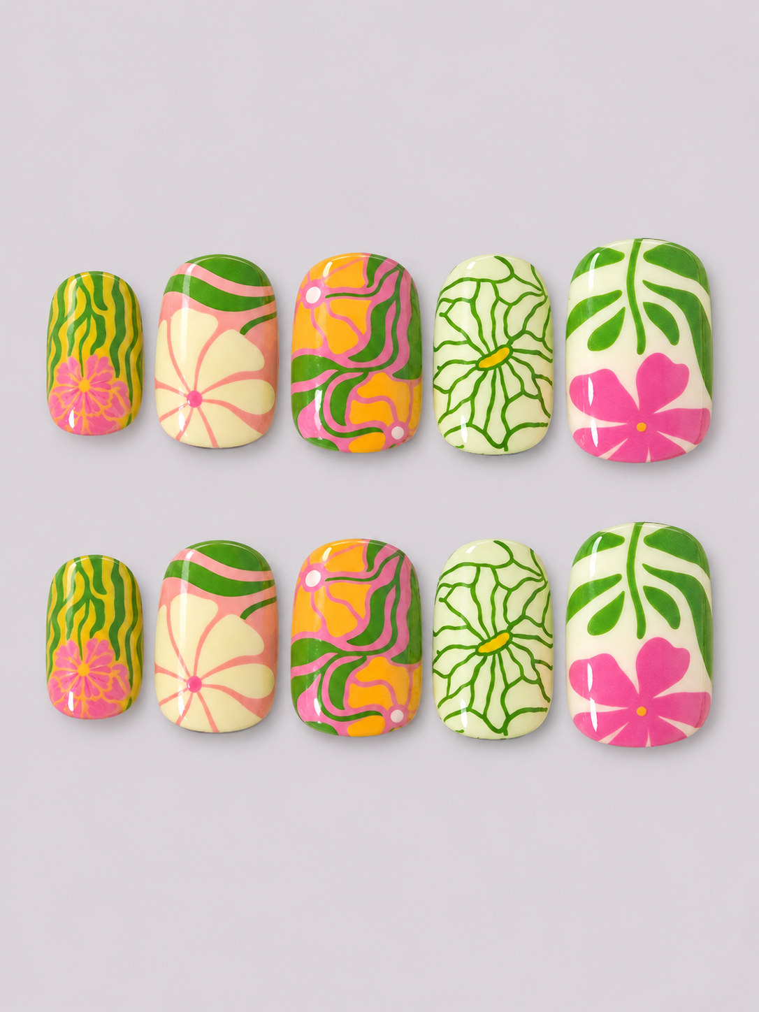 Ten artificial press-on nails arranged in two rows of five on a light gray background. The nails feature tropical floral and leaf patterns in bright pink, green, yellow, and cream.