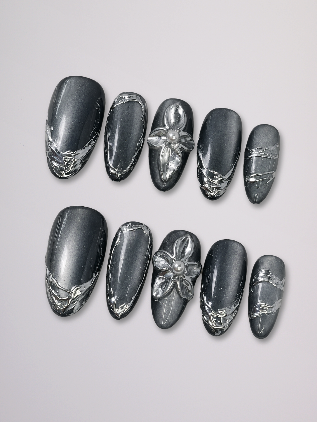 A close-up of a hand with long, glossy black stiletto-shaped nails decorated with silver butterfly and floral details, wearing a chunky silver ring with four oval purple gemstones, styled with a white shirt cuff against a light gray background.