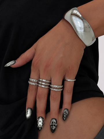 A close-up of a hand wearing multiple silver rings, a wide silver bangle bracelet, and silver nail art over a black top.