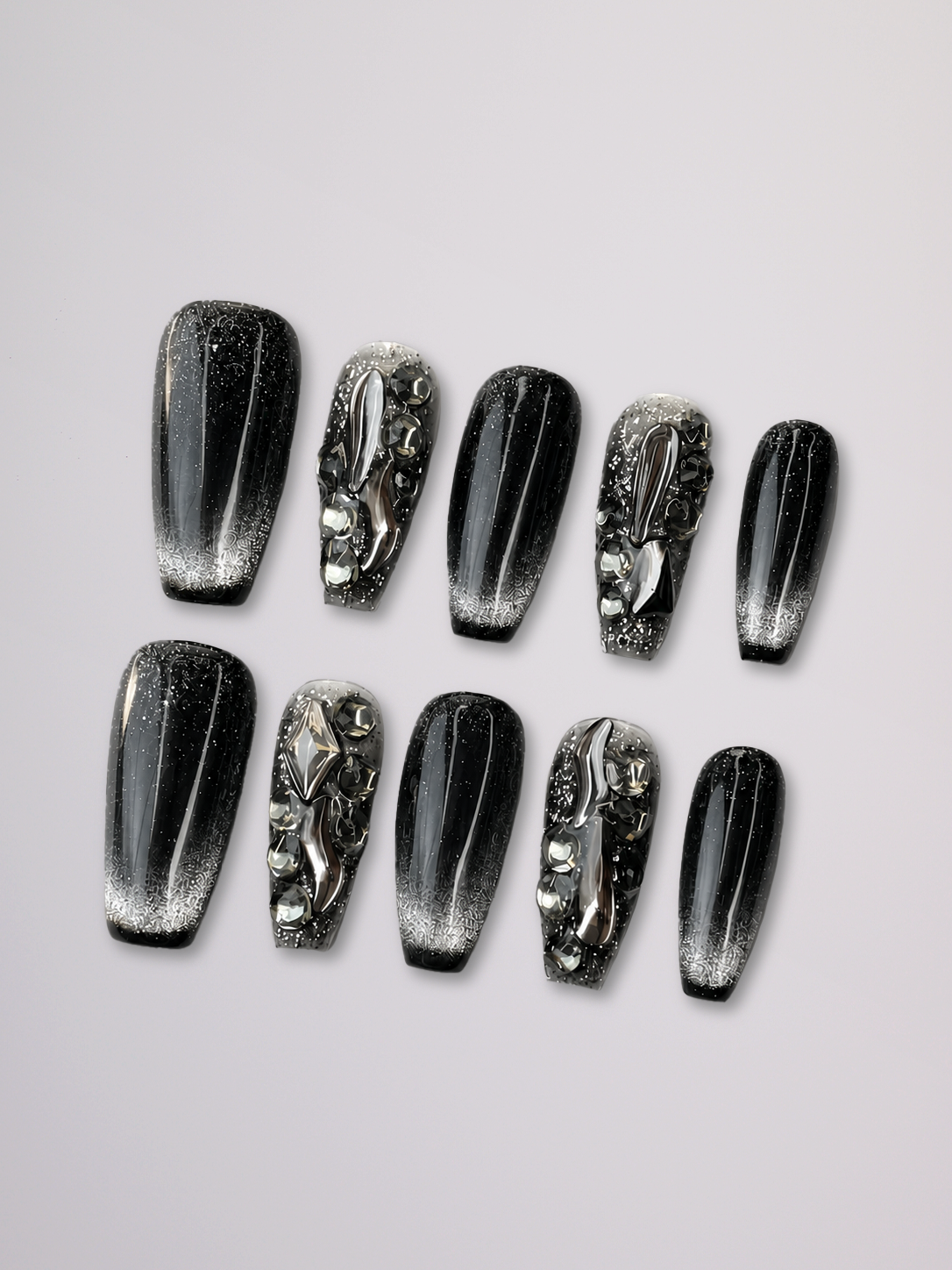 A set of ten coffin-shaped press-on nails arranged in two rows on a light gray background. The nails feature a glossy black and silver gradient with metallic glitter, rhinestone-like embellishments, and one nail with a raised silver animal motif.