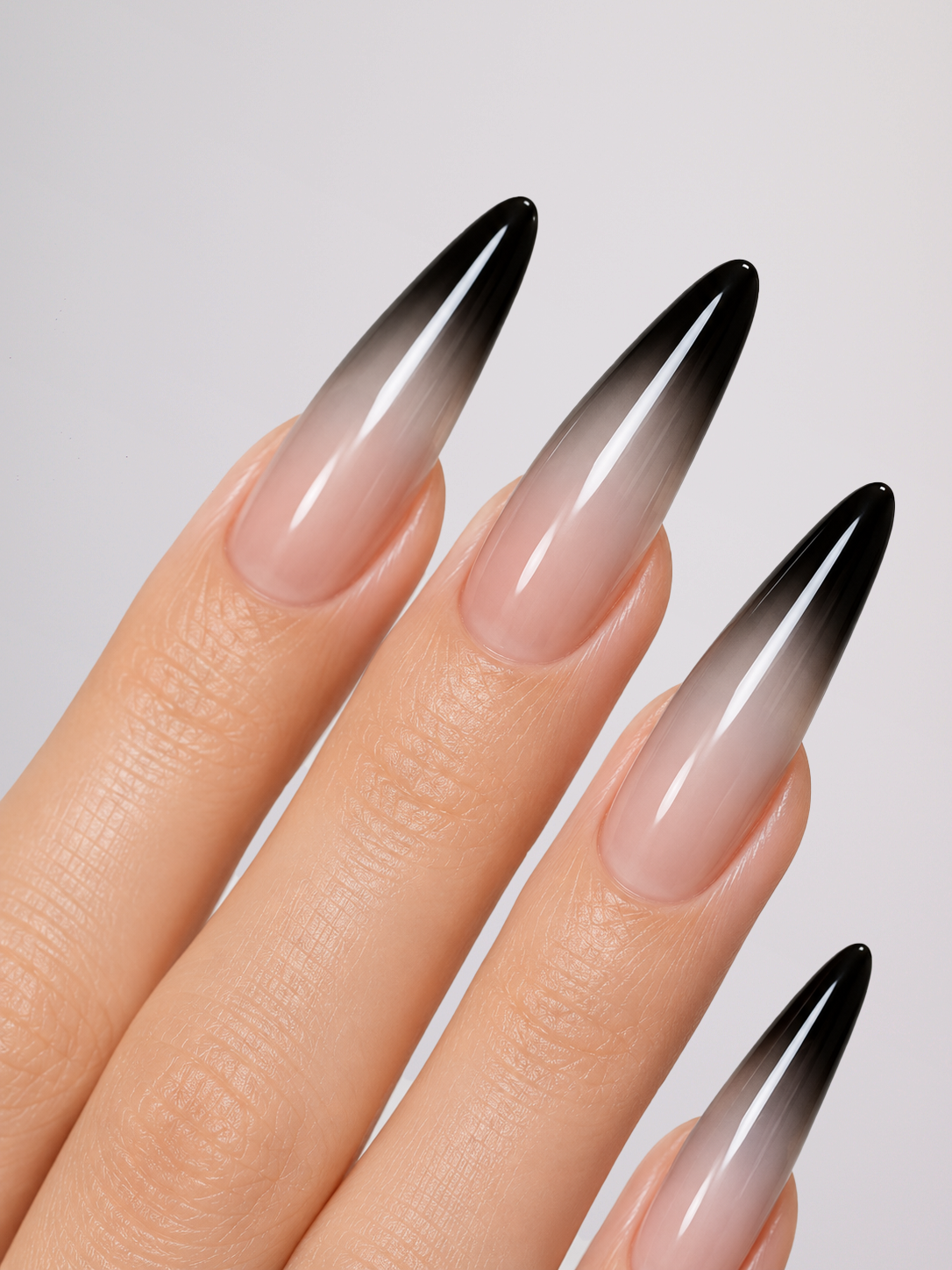 Long almond-shaped nails with a black-to-pale-pink ombre gradient, shown on hands against a light gray background.