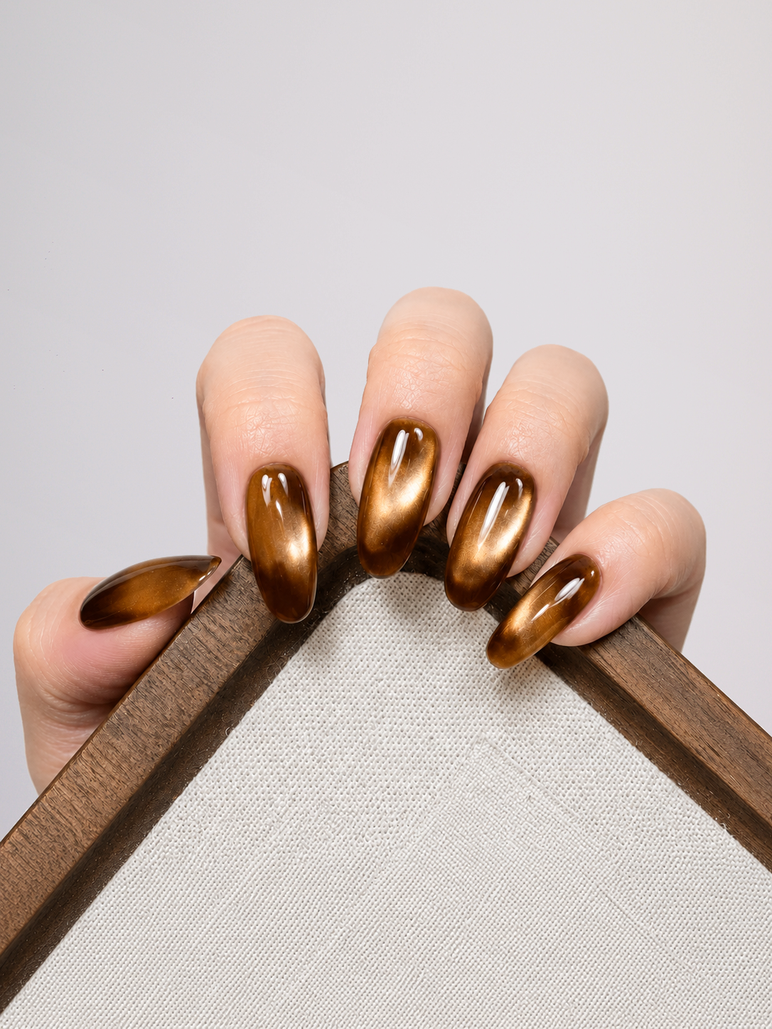 Two hands with metallic bronze nail polish, posed against a solid light gray background.