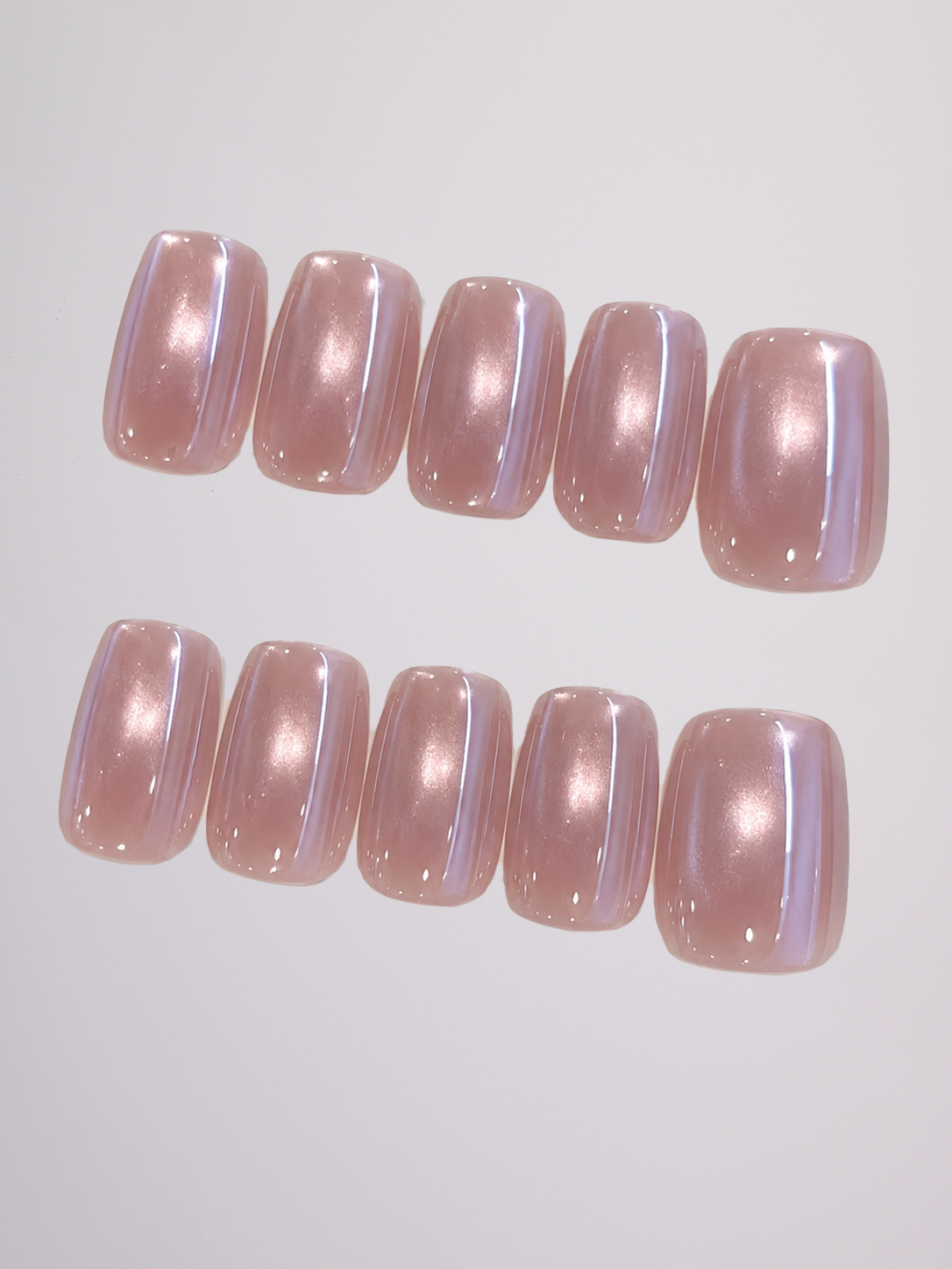 Ten false nail tips in a glossy, iridescent pale pink color with a subtle purple sheen, arranged in two rows of five on a light gray background.