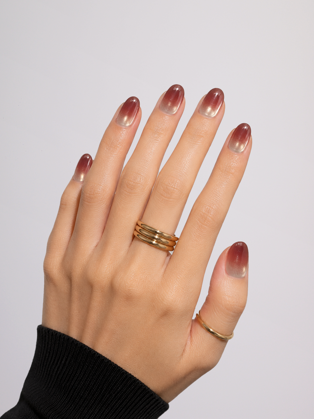 A close-up of a person's hands and shoulder wearing two gold rings. One ring features multiple stacked horizontal bands, and the other is a smooth, polished band ring.