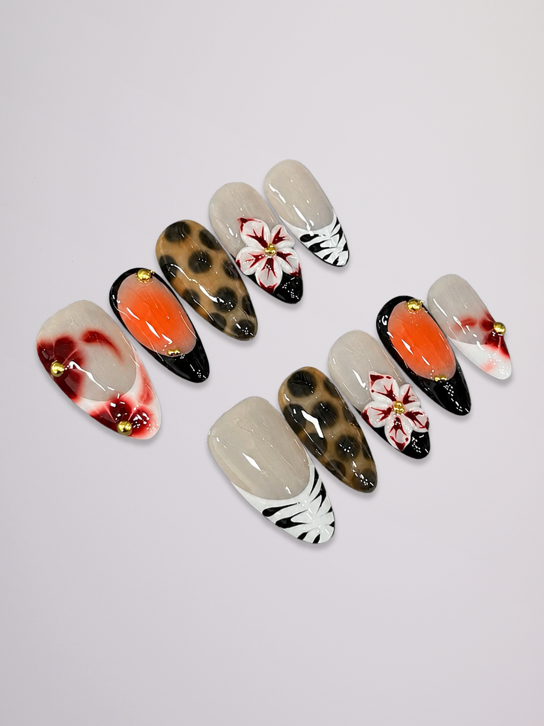 A set of artificial press-on nails arranged on a light gray background. The nails feature various designs including solid orange, leopard print, white with red floral details, black and white zebra stripes, and glossy beige.