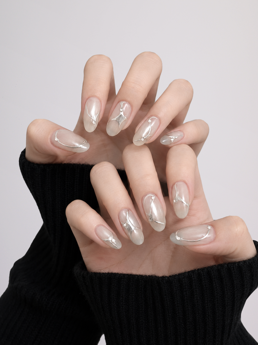 Hands wearing Silver Current press-on nails with flowing silver chrome lines and bead details over a translucent milky base.