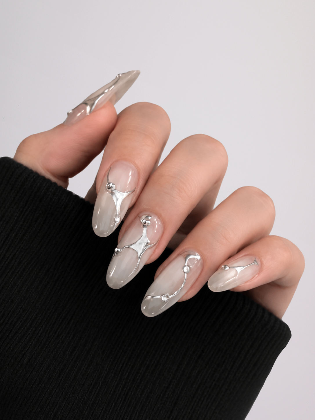 Close-up of Silver Current press-on nails showing raised silver chrome lines and bead details, worn with a black sleeve.