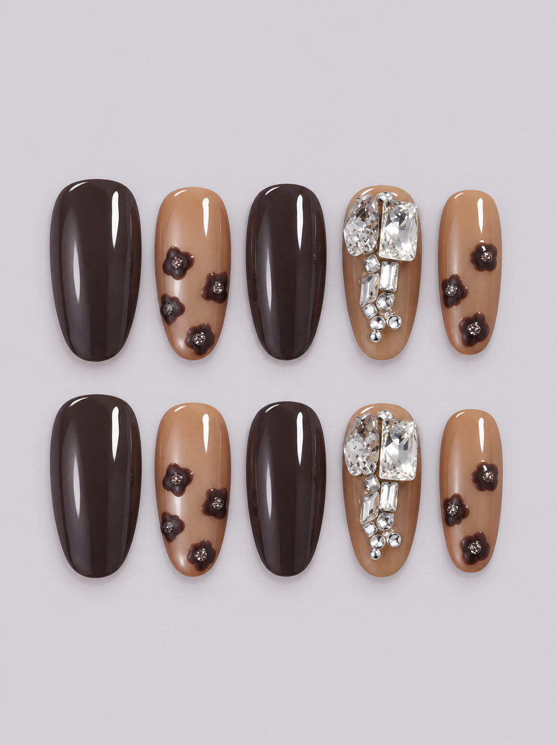 A close-up of a hand with long almond-shaped nails styled in a brown and nude glitter manicure, wearing a dark brown knit sweater and silver rings against a light gray background.