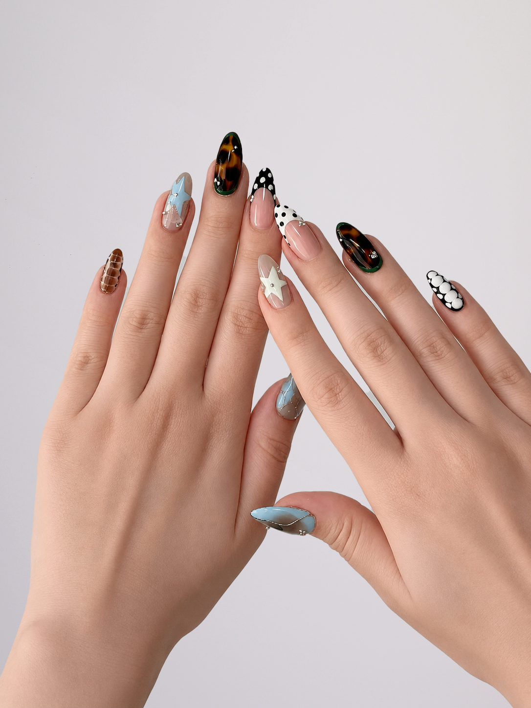 Hands wearing mixed-print almond press-on nails with leopard, polka dot and star designs