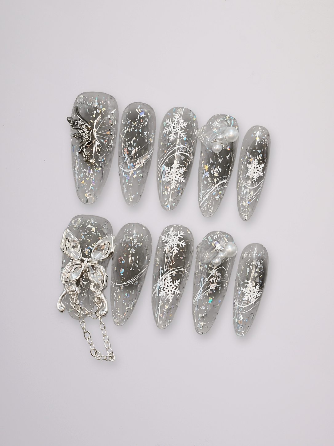 A set of ten clear press-on nails decorated with silver glitter, white snowflakes, and silver butterfly embellishments, arranged on a light gray background.