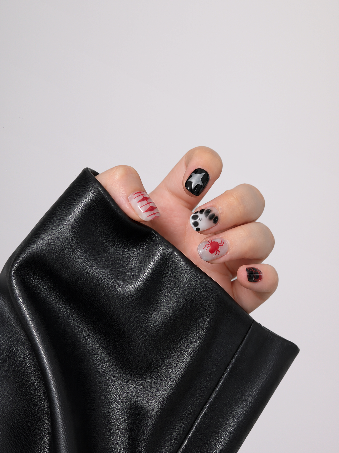 A close-up of a hand with decorated nails resting against a black faux-leather sleeve, set against a plain light gray background.
