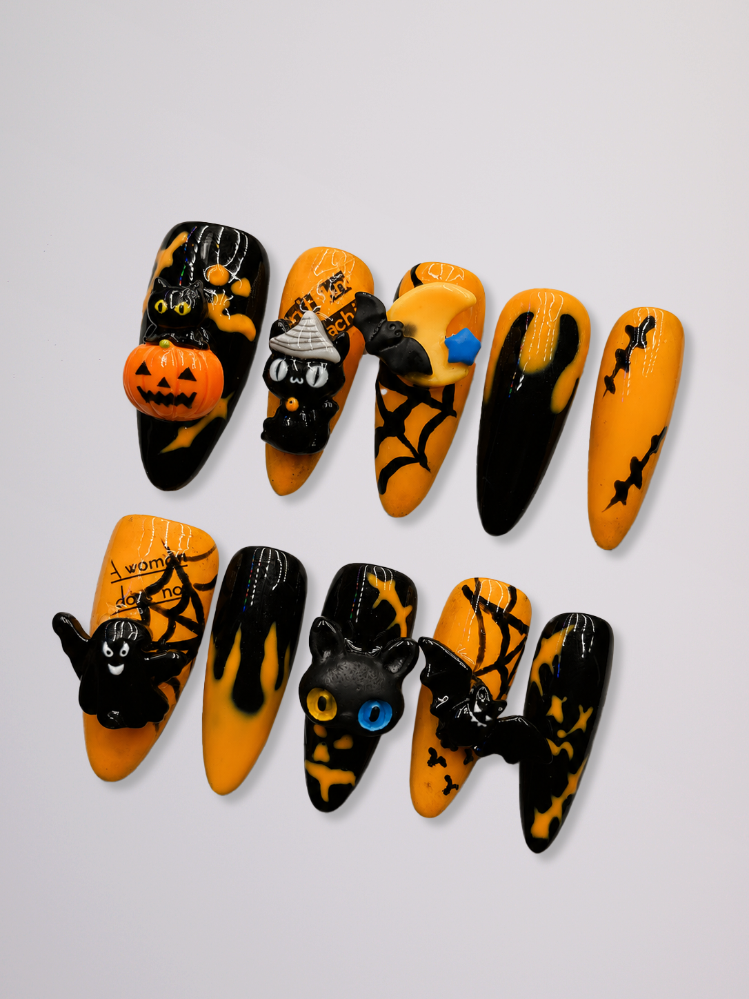A set of ten coffin-shaped press-on nails with Halloween designs, including pumpkins, cats, spiders, and bats in black and orange, displayed on a light gray background.