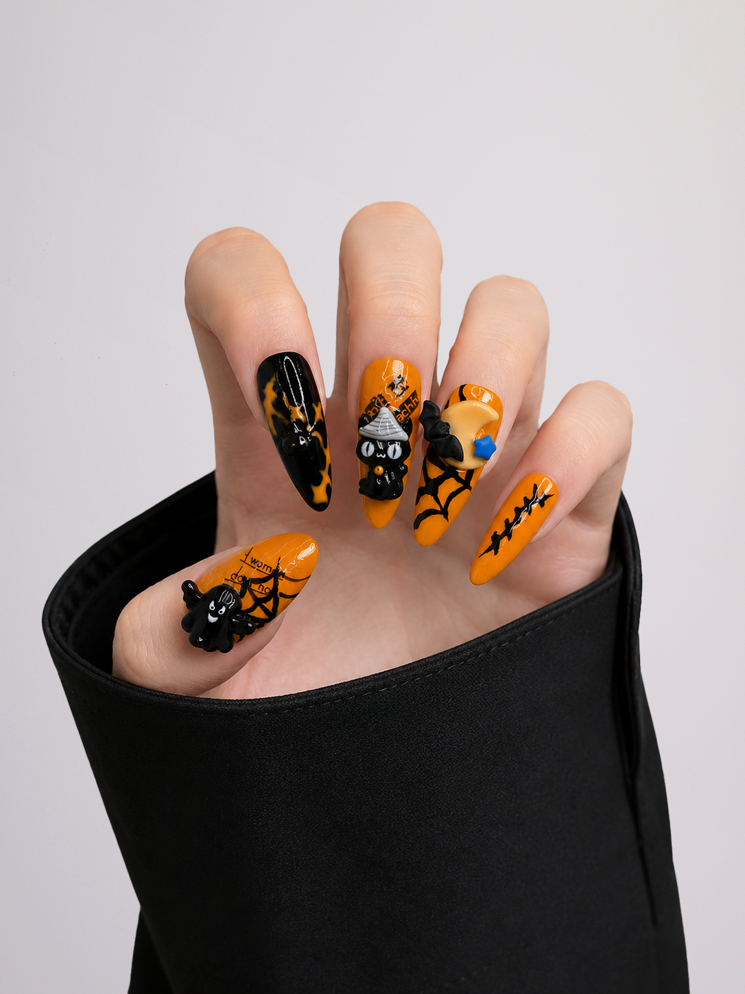 A set of ten coffin-shaped press-on nails with Halloween designs, including pumpkins, cats, spiders, and bats in black and orange, displayed on a light gray background.