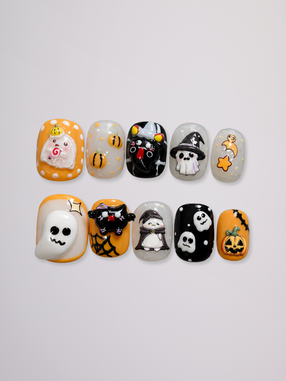 A set of ten Halloween-themed press-on nails arranged in two rows on a light gray background. The designs include ghosts, pumpkins, witches, spiders, and spiderwebs in orange, black, white, and gray.