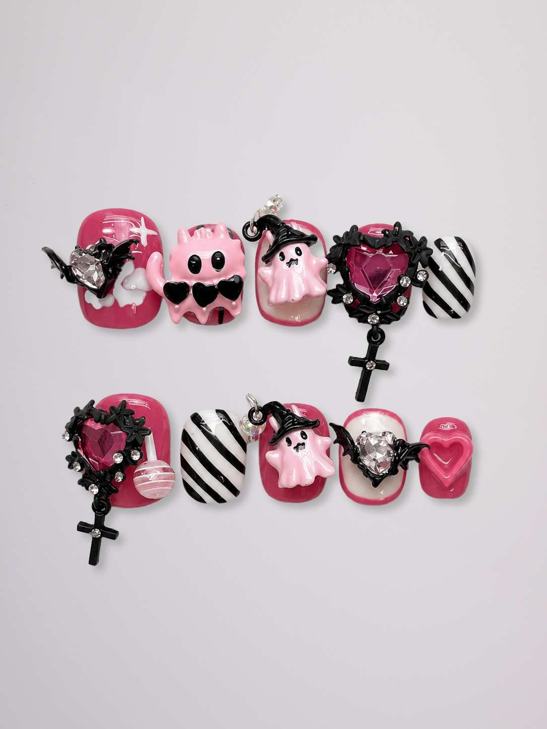 A set of Halloween-themed press-on nails arranged in two rows on a light gray background. The nails feature pink and white ghost designs, black and white striped patterns, and gothic black lace details with small silver rhinestones and crosses.