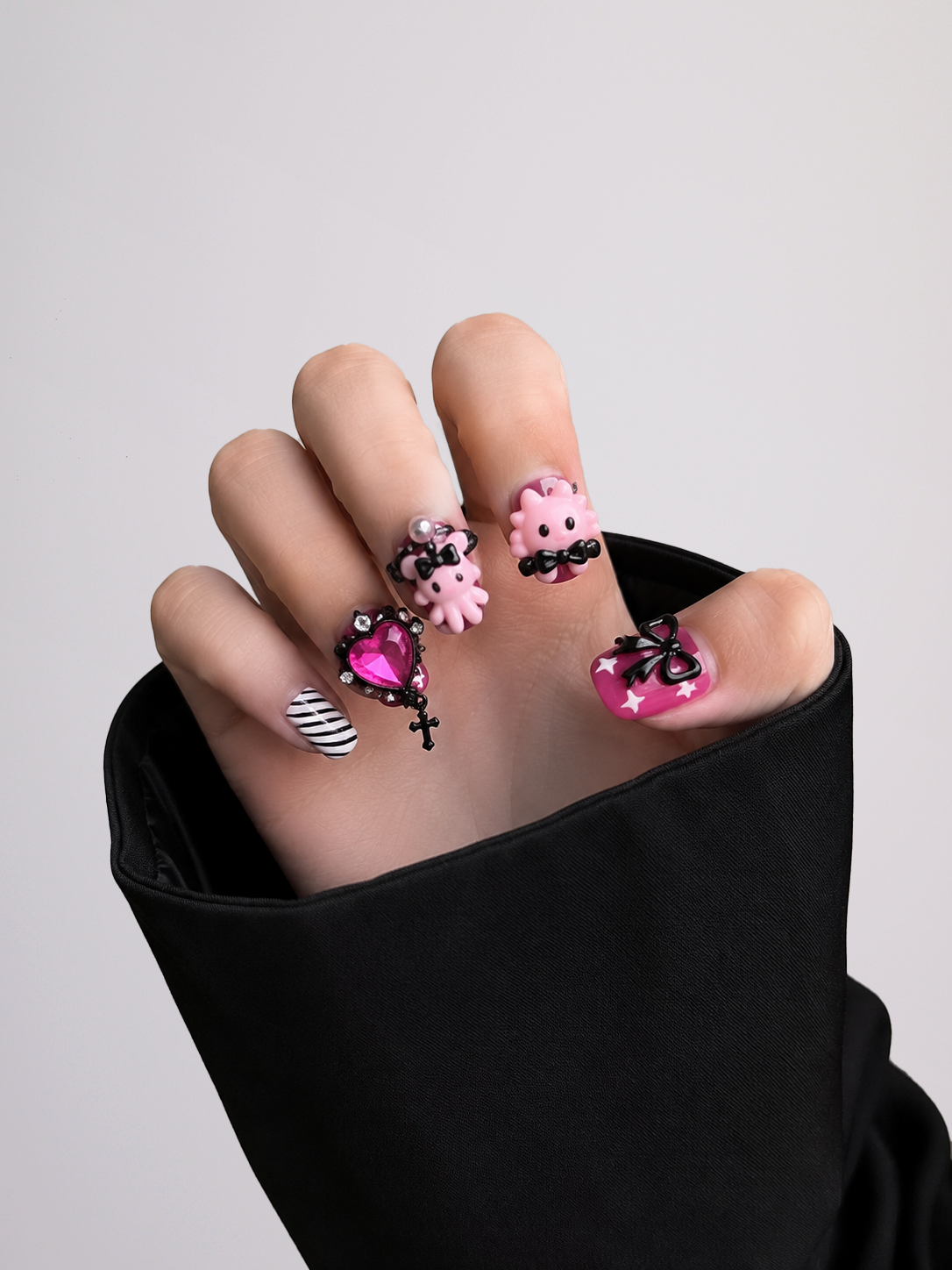 A set of Halloween-themed press-on nails arranged in two rows on a light gray background. The nails feature pink and white ghost designs, black and white striped patterns, and gothic black lace details with small silver rhinestones and crosses.