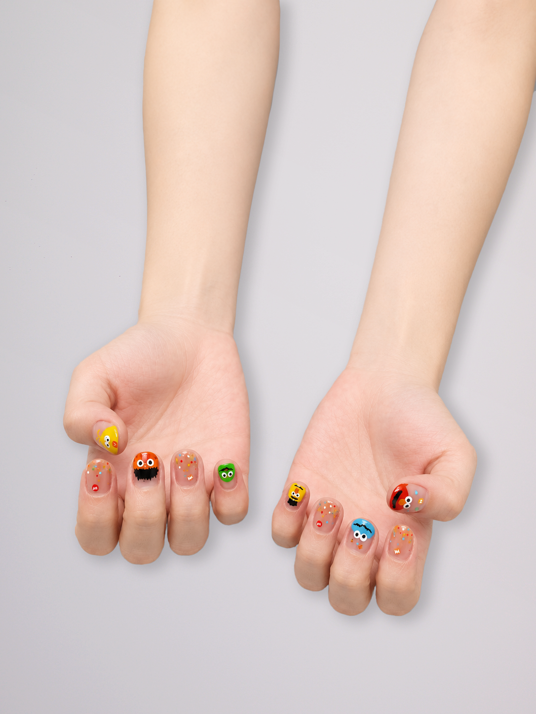 A pair of hands with colorful cartoon-themed nail art, shown against a plain light gray background.