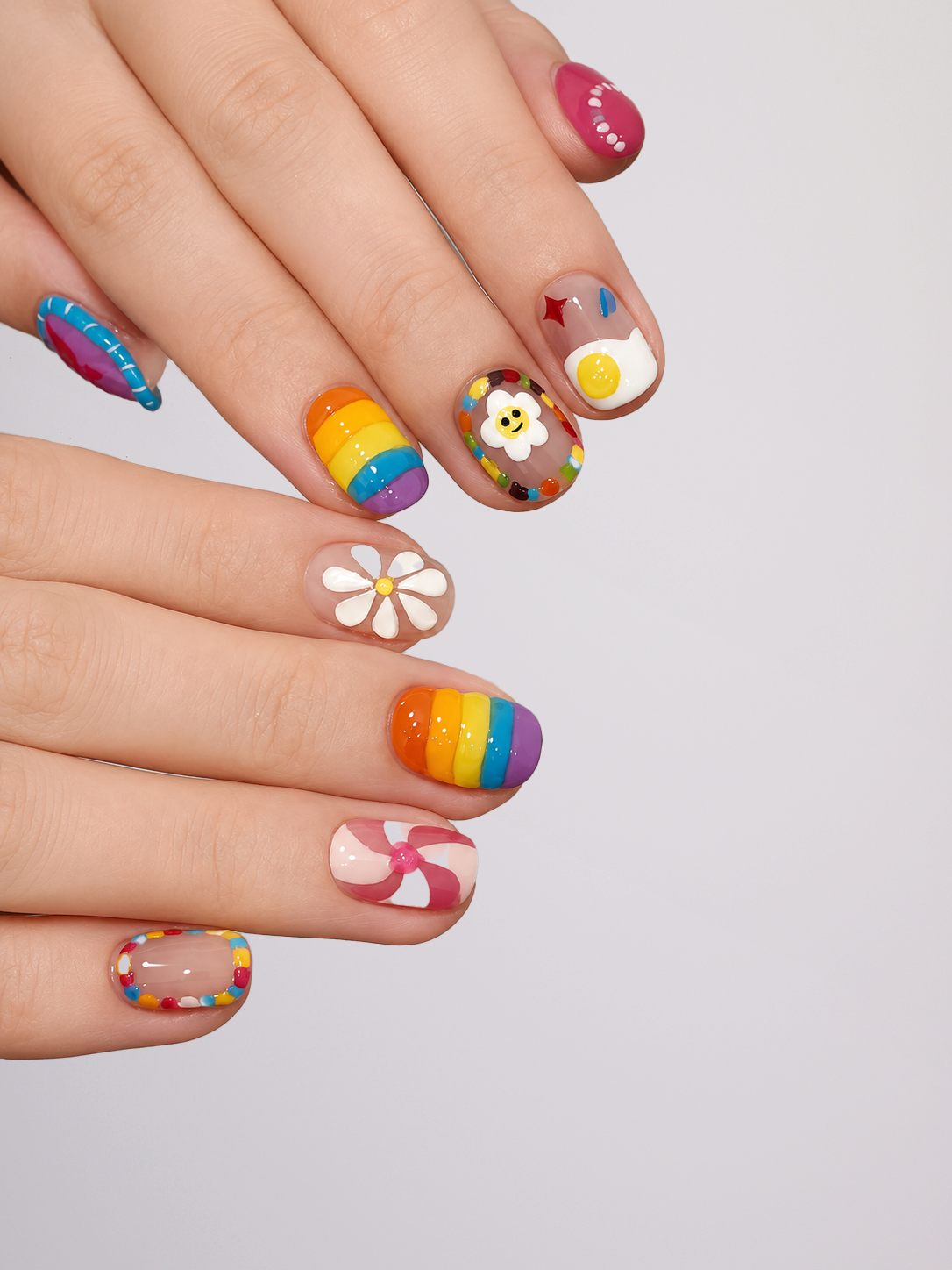 A close-up of hands showcasing a variety of colorful, creative nail art designs on a light gray background.