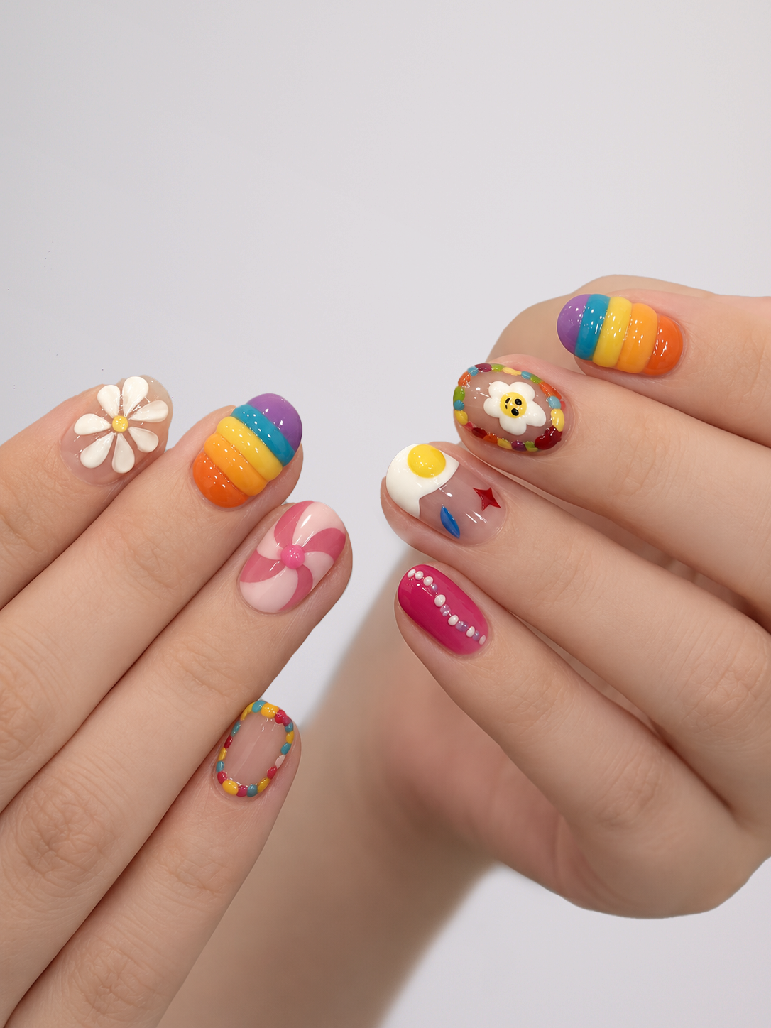 A close-up of hands showcasing a variety of colorful, creative nail art designs on a light gray background.