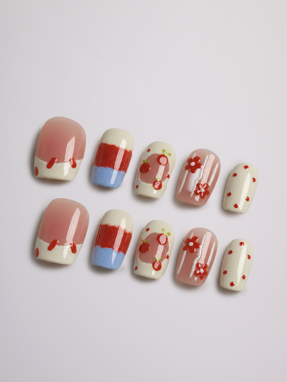 A set of ten press-on nails arranged in two rows on a light gray background. The nails feature a mix of designs including solid pinkish nude, cream with red stripes, cream with red flowers, and cream with red dots.