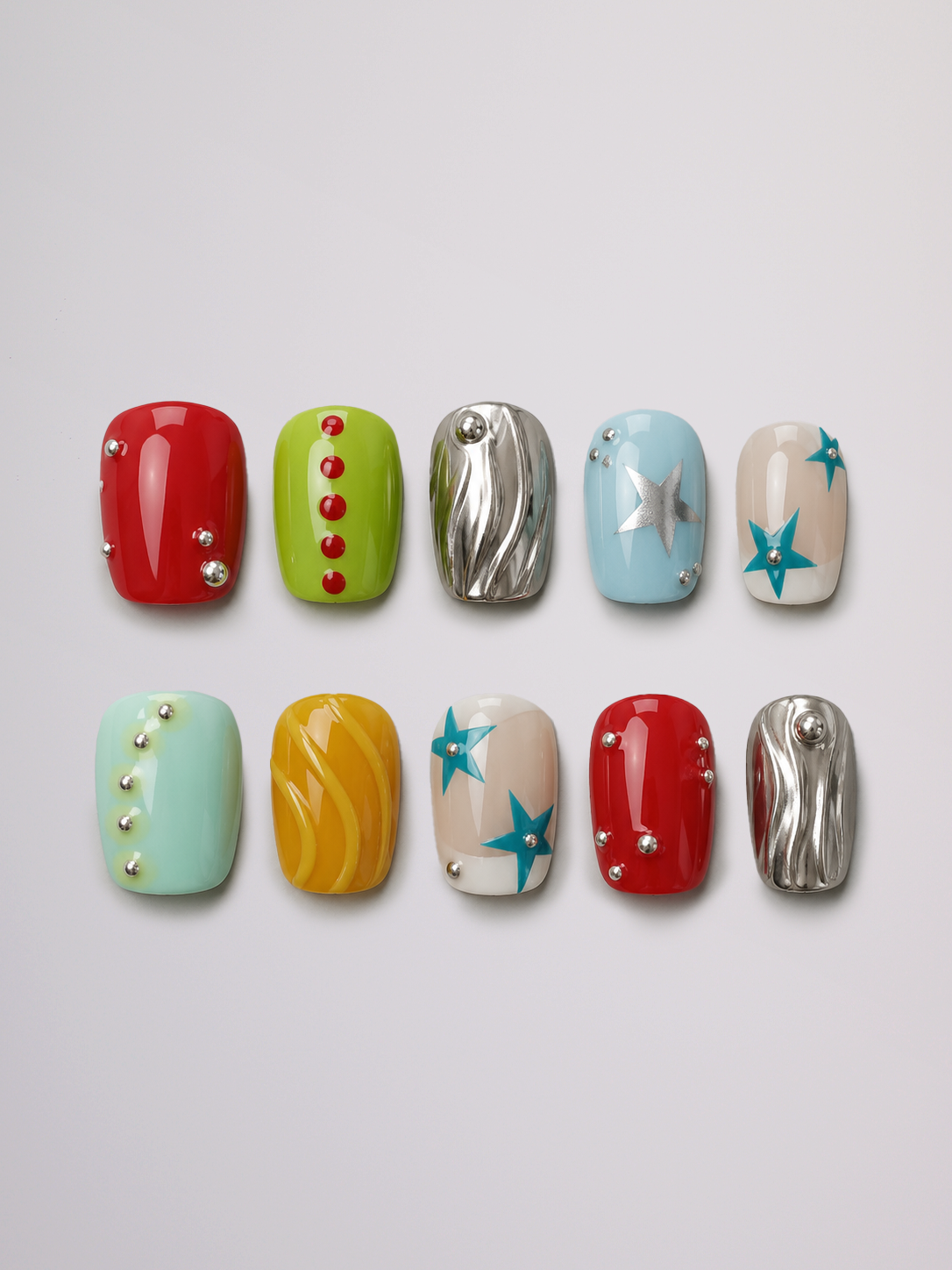 Ten artificial nail tips arranged in two rows on a light gray background, each with a different decorative nail art design including red, green, silver, blue, beige, mint, yellow, and white patterns.