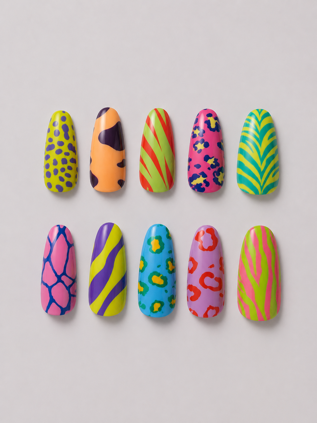 A pair of hands with long stiletto-shaped nails decorated in vibrant, multicolor patterns including pink flowers, green spots, blue and yellow stripes, and purple leopard print, styled with gold rings against a light gray background.