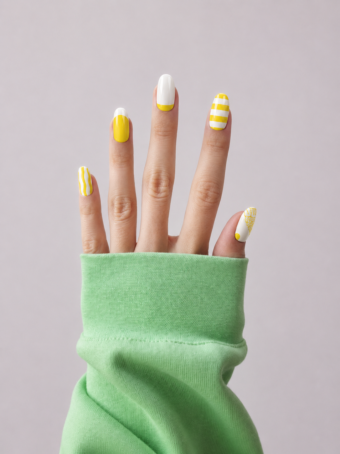 A close-up of a hand with yellow and white manicured nails, wearing a light green long-sleeve top against a solid light gray background.