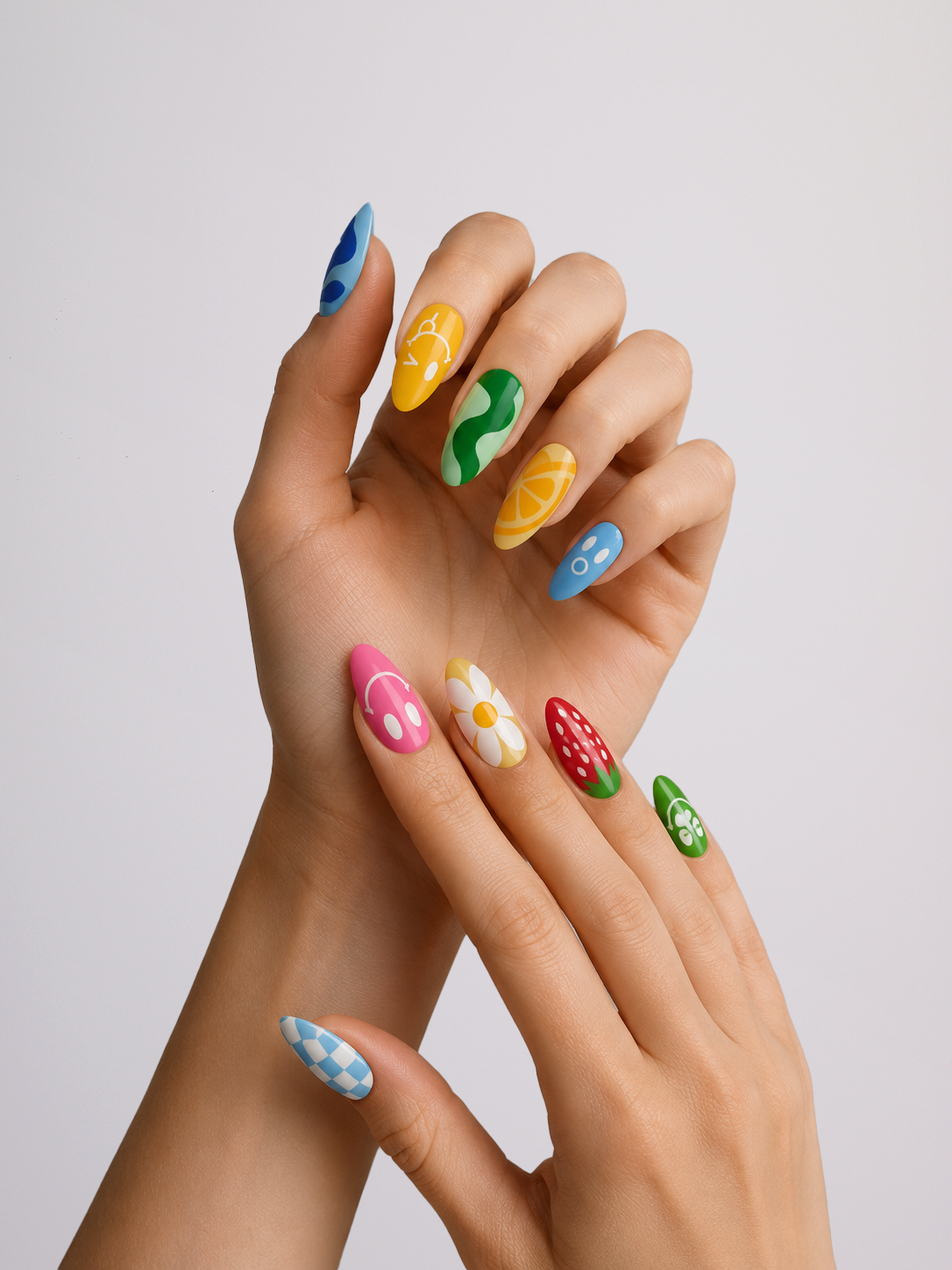 A close-up of hands showcasing colorful, decorative press-on or nail art nails with various patterns like stripes, dots, and flowers in blue, yellow, green, pink, red, and white against a light gray background.