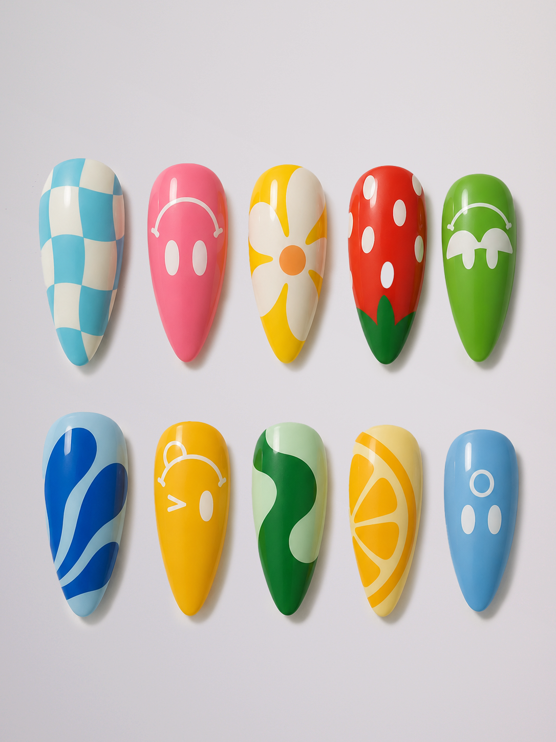 A close-up of hands showcasing colorful, decorative press-on or nail art nails with various patterns like stripes, dots, and flowers in blue, yellow, green, pink, red, and white against a light gray background.
