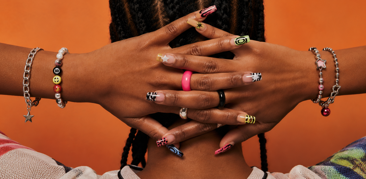 Close-up of hands with colorful nail polish and bracelets against an orange background